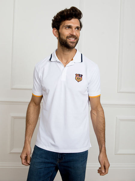 Man wearing white polo shirt in 100% cotton with Newmarket 875 crest embroidered on the front with navy sleeve trimming and gold collar trimming.